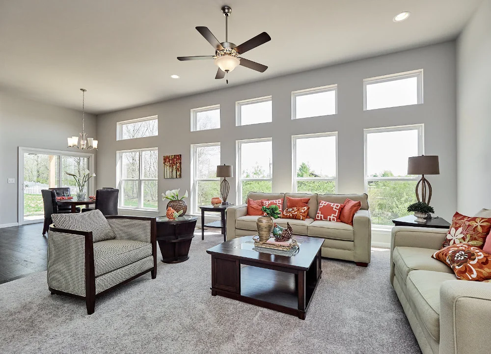 A new home living room with 11" ceilings, small transom windows at the top, light, earthtone furniture, and a ciling fan.