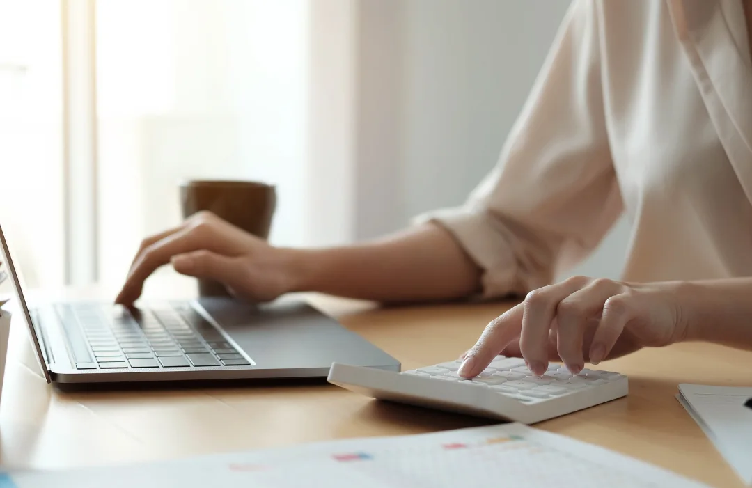 Woman with one hand working a calculator and the other a laptop
