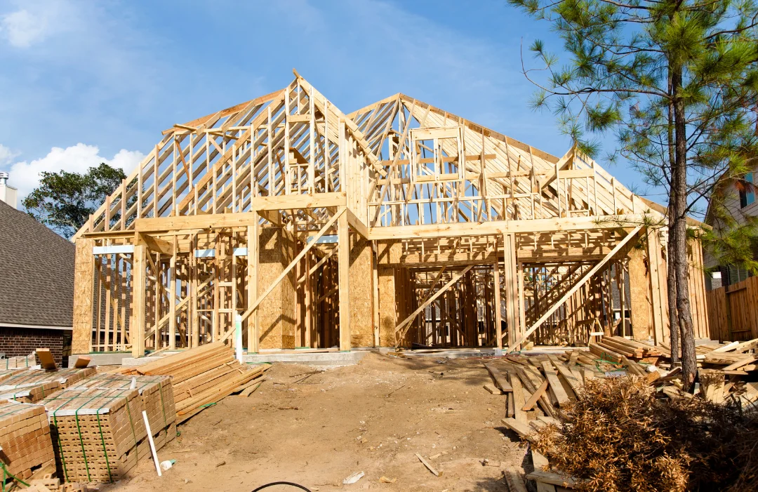 CMS-New-Construction-Home A house frame newly constructed on a dirt lot with a pine tree out front.