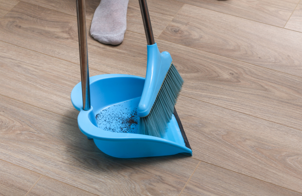 A person in socked feet with a broom and dustpan sweeping up dirt on a wood floor.